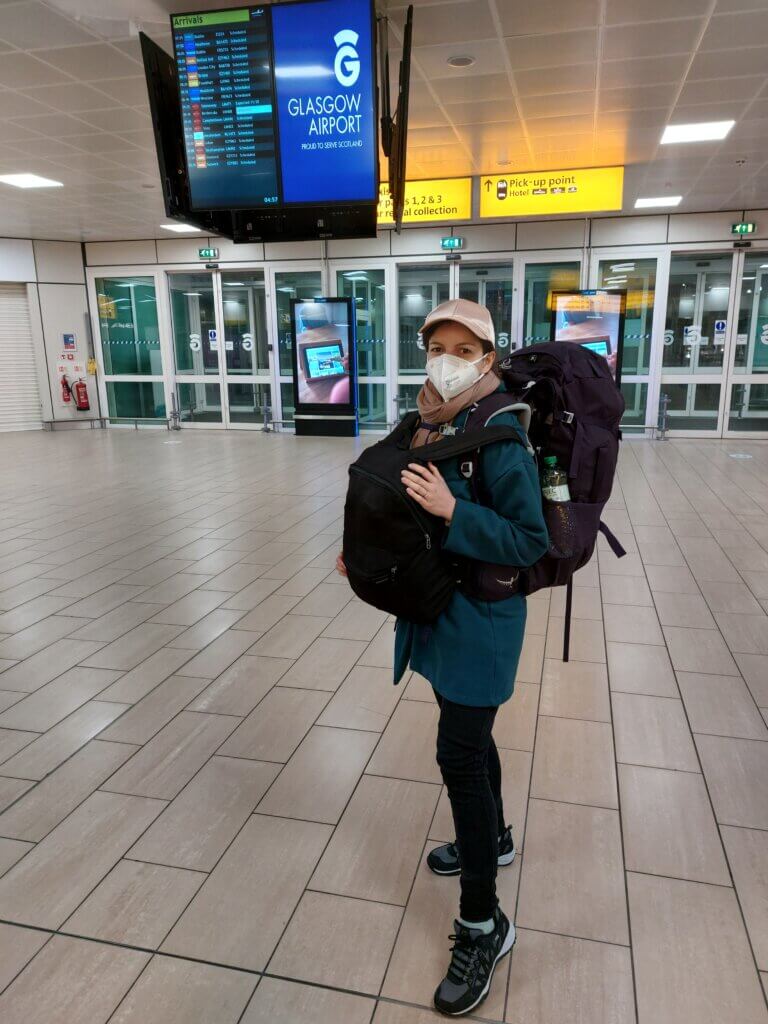 Mirka standing inside of an airport wearing a face mask and a big Osprey backpack at the back and a small daybag at the front.