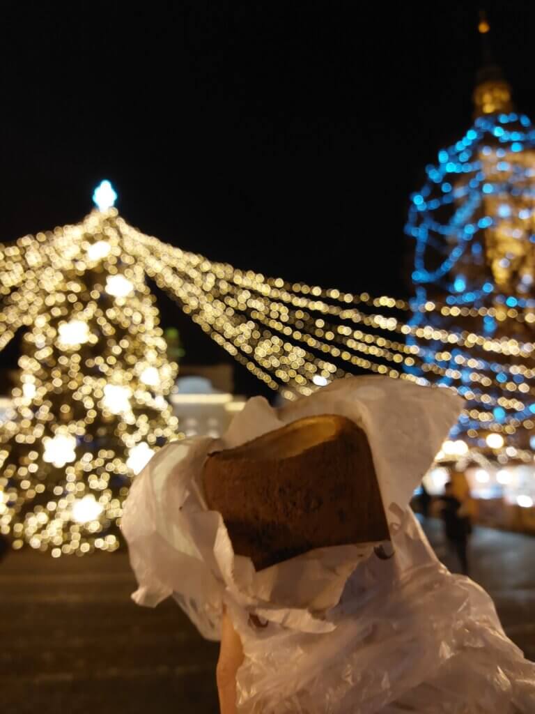 Chimney cake held up with a blurry Christmas tree and other Christmas lights in the background