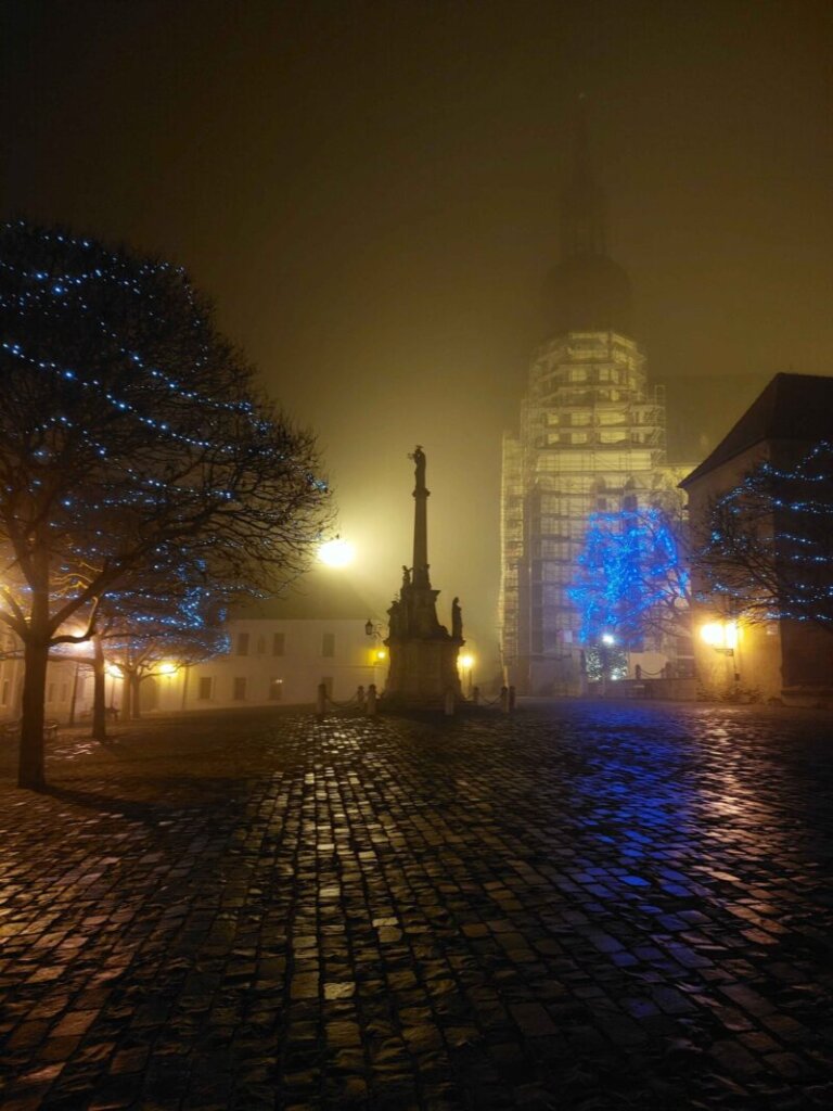 A foggy cobbled square with a church under construction in the background