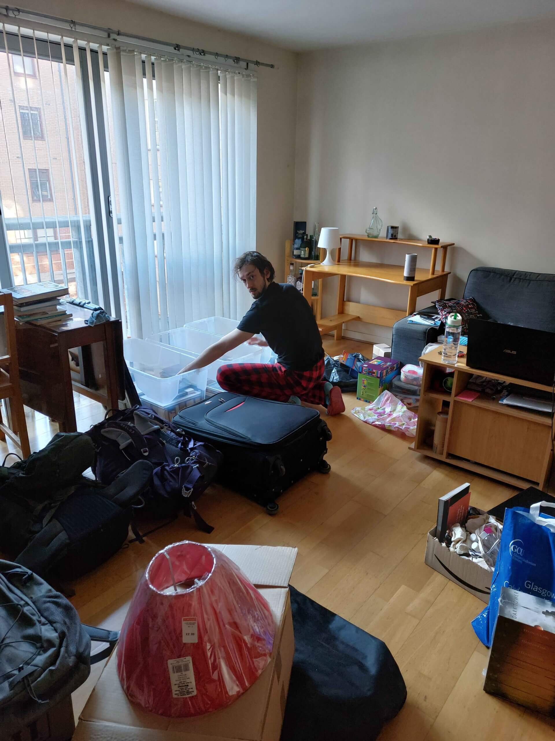 Daniel crouching in a living room surrounded by boxes, suitcases and stuff