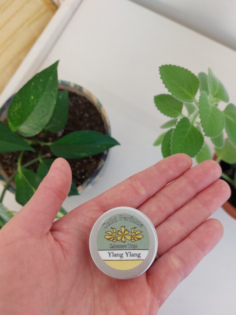 A small round tin of solid perfume held in a hand