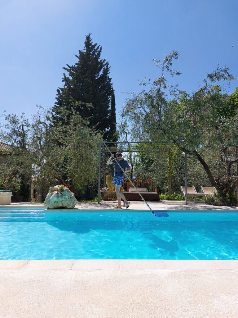 Daniel standing on an edge of a pool in a garden in Italy, cleaning it