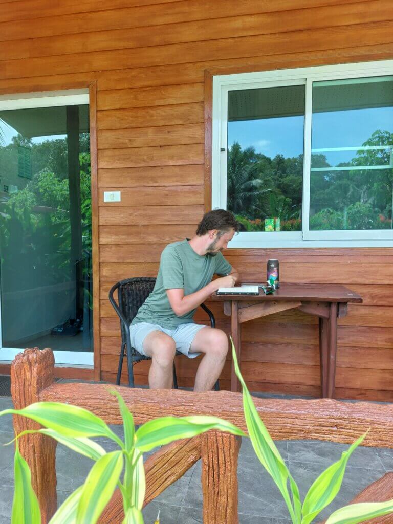 Daniel sitting at a wooden table outside a wooden bungalow writing a journal