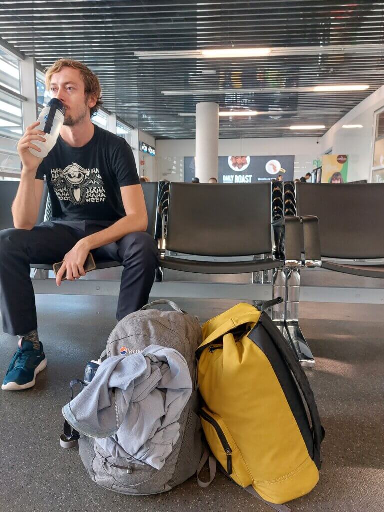 Daniel sitting at an airport with two small daybags at his feet