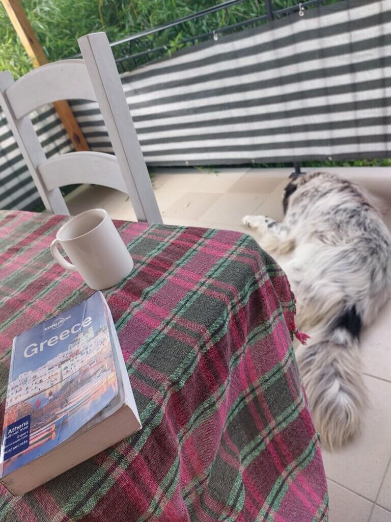 A Lonely Planet guide to Greece lying on a table with a big fluffy dog lying next to it.