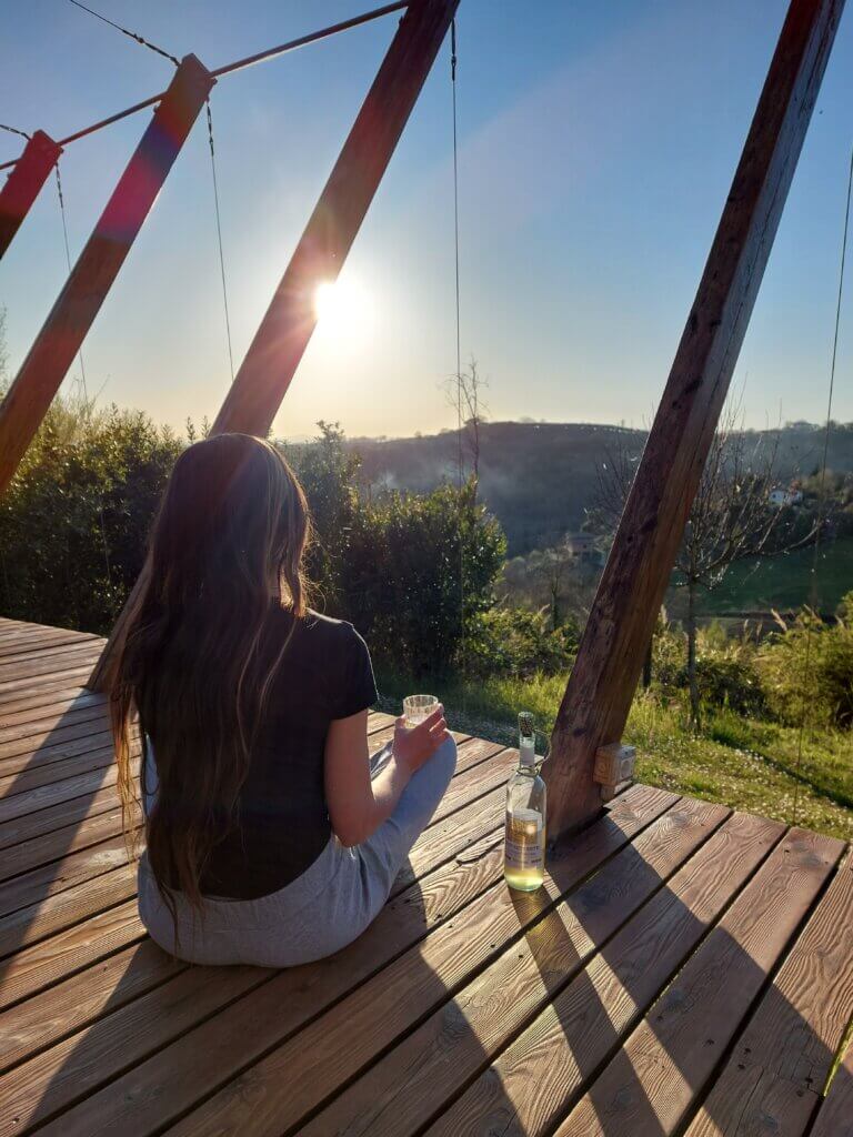 Mirka sitting on a wooden platform overlooking Italian countryside with a glass of wine in her hand.