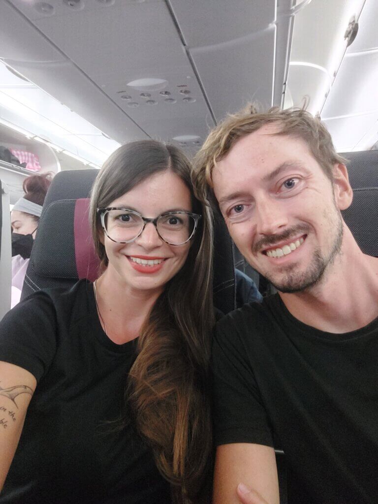 Mirka and Daniel taking a selfie on a long-haul flight. We are smiling because we use long-haul flight hacks to make the flight a more enjoyable experience.