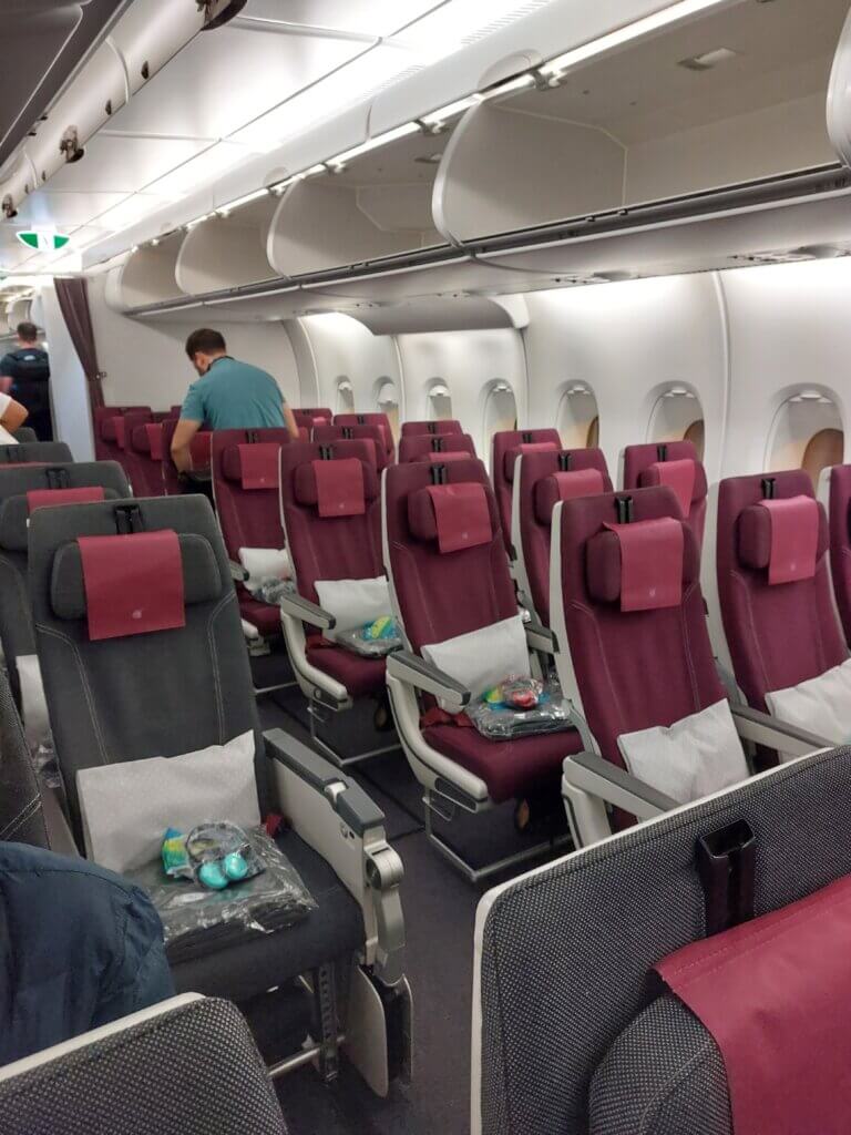 A photo of seats on a plane on a long-haul flight with one having an extra legroom because of another seat missing in front of it