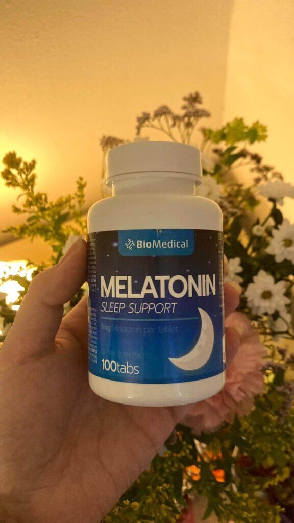 A bottle of melatonin pills being held up with flowers in the background