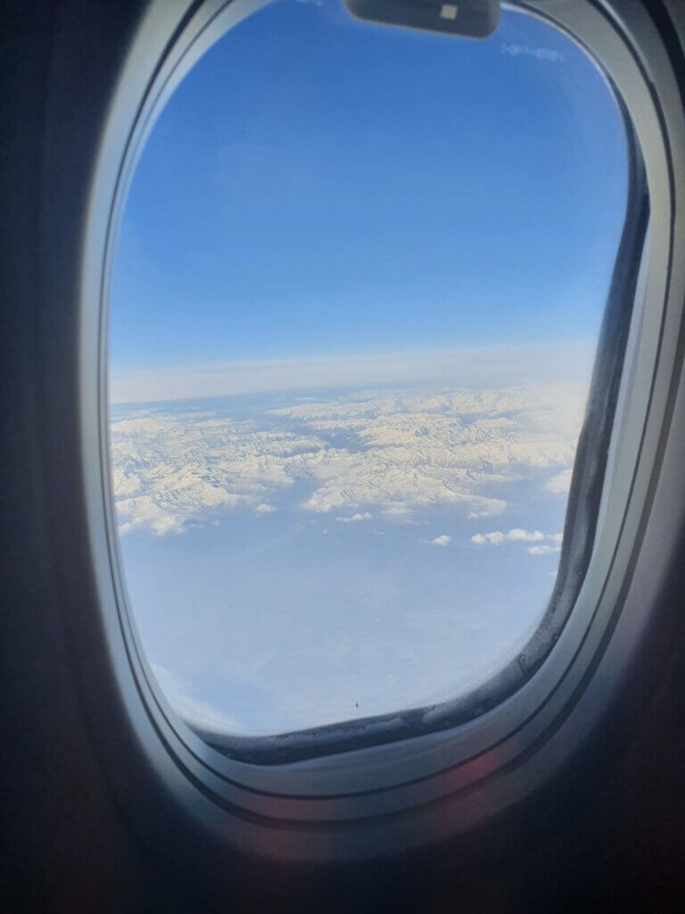 A plane window with a view of bare mountains below