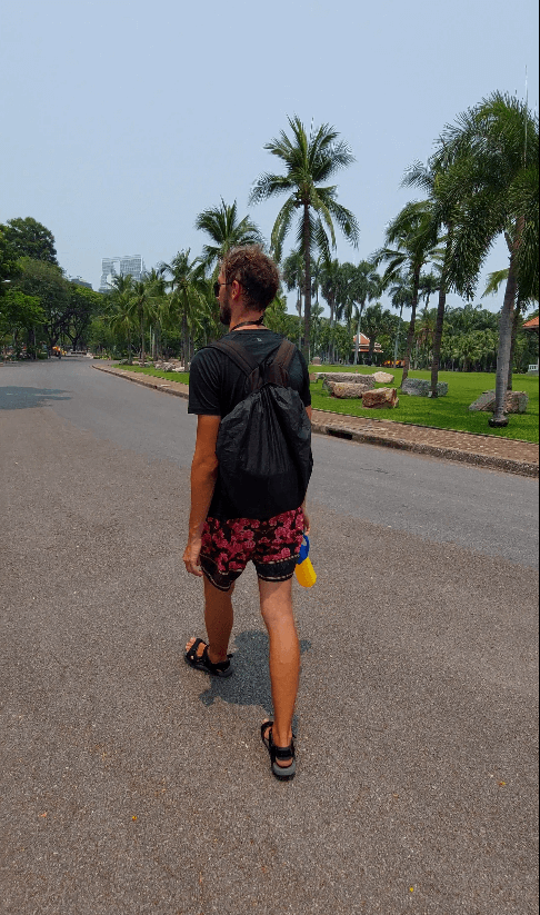 Daniel walking through the Lumphini Park holding a water gun and wearing a black backpack with a black raincover
