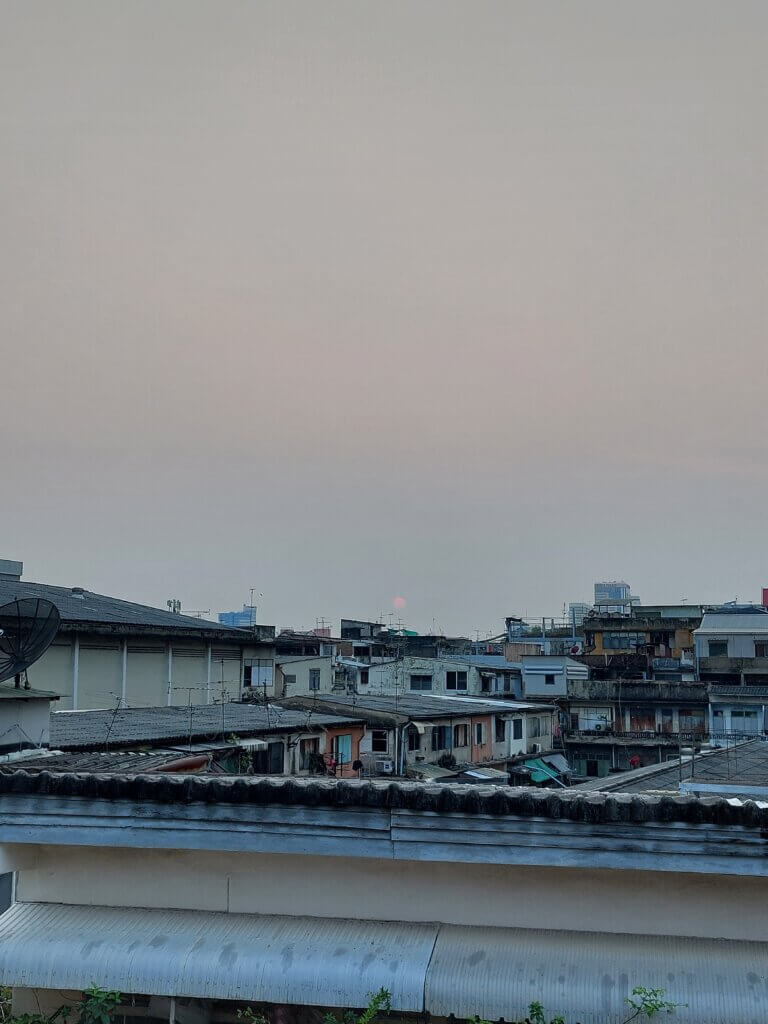 A view over Bangkok from a rooftop with a red sun setting in the distance