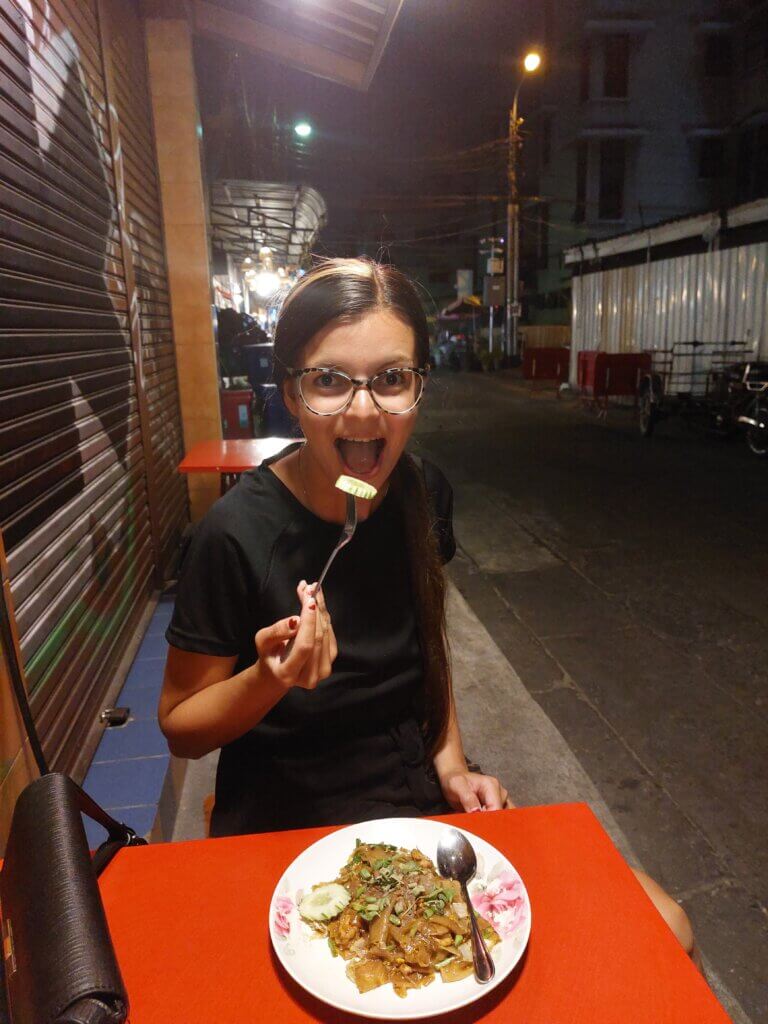 Mirka sitting on a street at a red table eating noodles