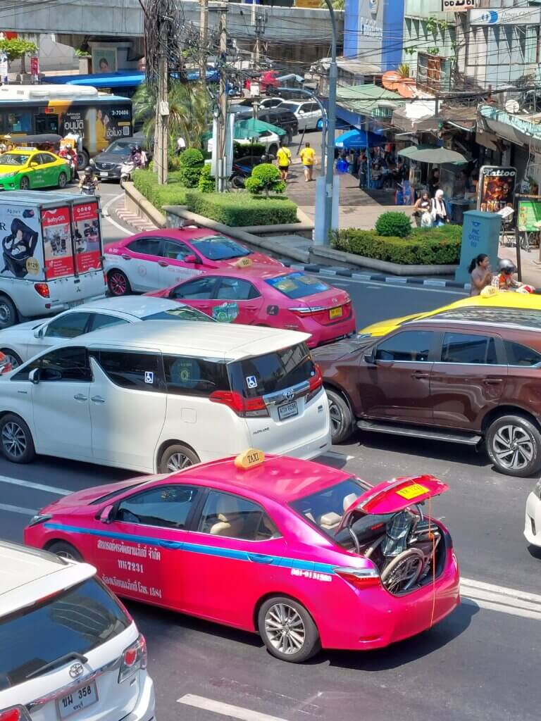 Bangkok traffic jam with a pink taxi with an open booth and a wheelchair peaking out