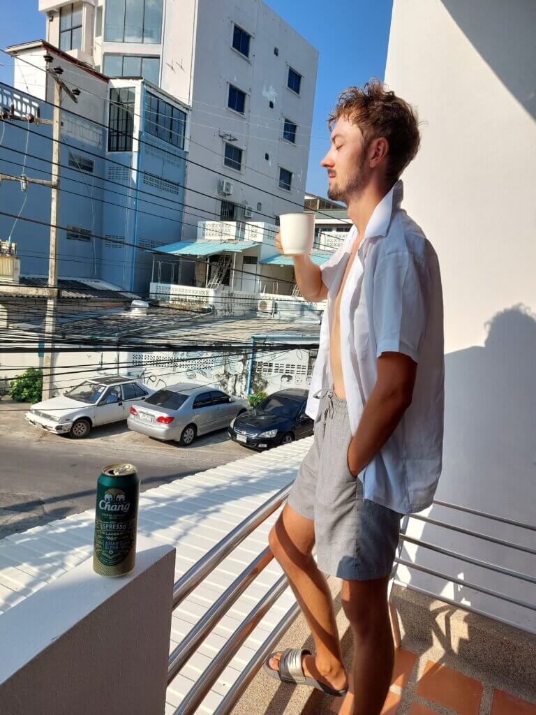 Daniel standing on a balcony with his eyes closed and a cup of coffee in his hand