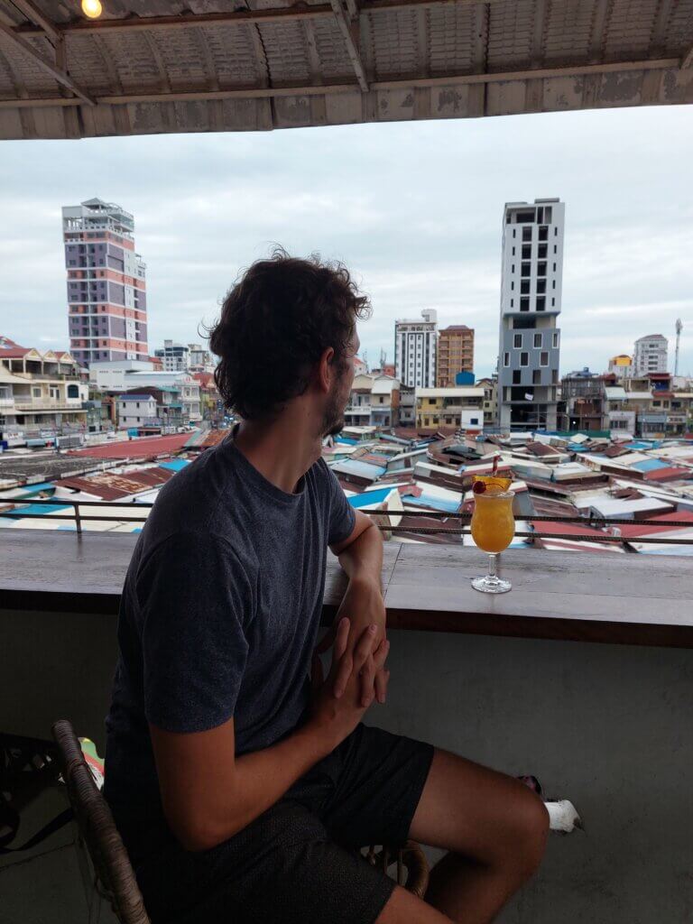 Daniel sitting on a bar balcony overlooking rooftops with a cocktail in front of him