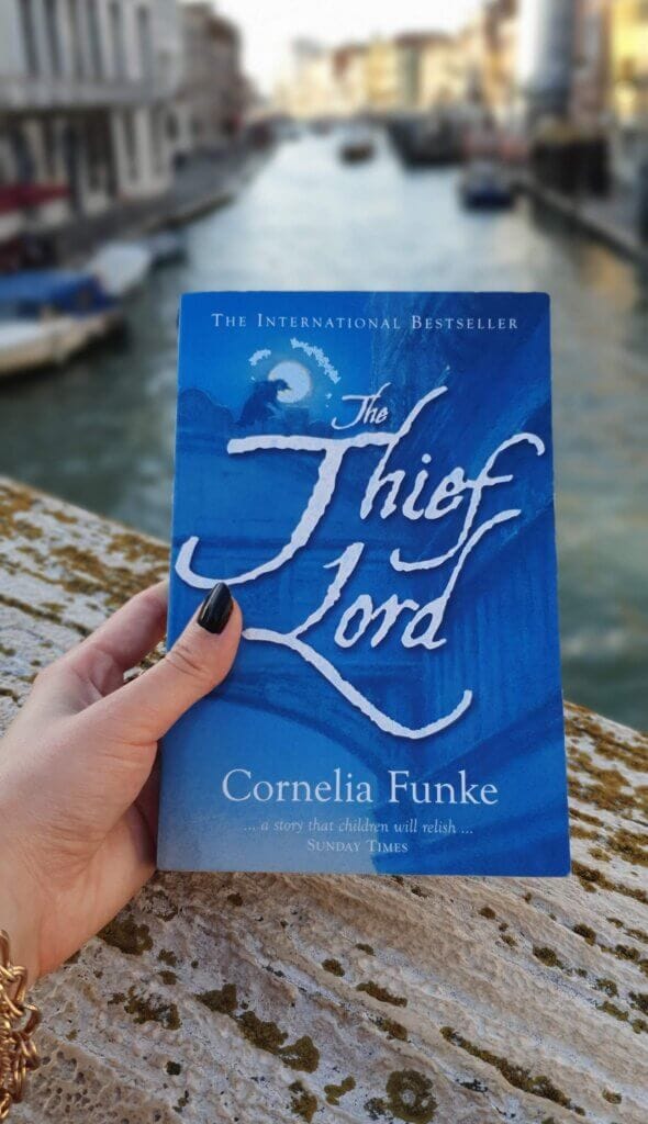 A copy of The Thief Lord book held up against a backdrop of Venice