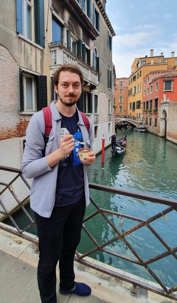Daniel standing on a bridge over a canal with a tub of tiramisu in his hand