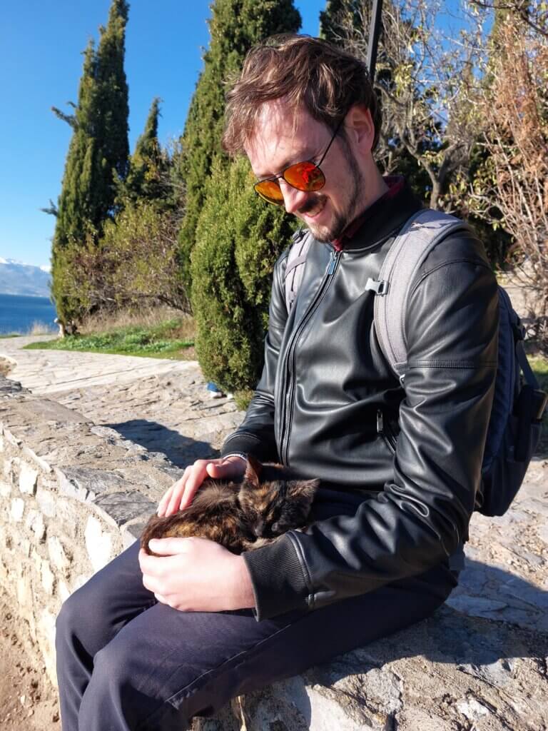 Daniel sitting on a stone wall with a cat asleep on his lap