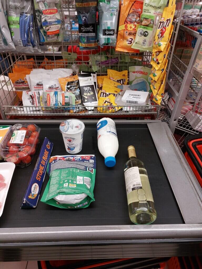 Yoghurt, milk, bag of granola and a bottle of wine on a conveyor belt at a till.