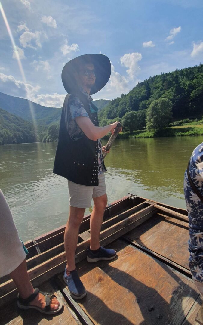 Daniel wearing a traditional hat and a vest while steering a wooden raft -  - one of the unusual things to do in Slovakia