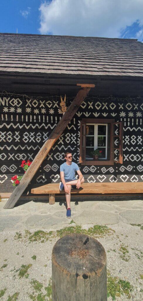 Daniel sitting in front of a folkore-painted house in the village Cicmany