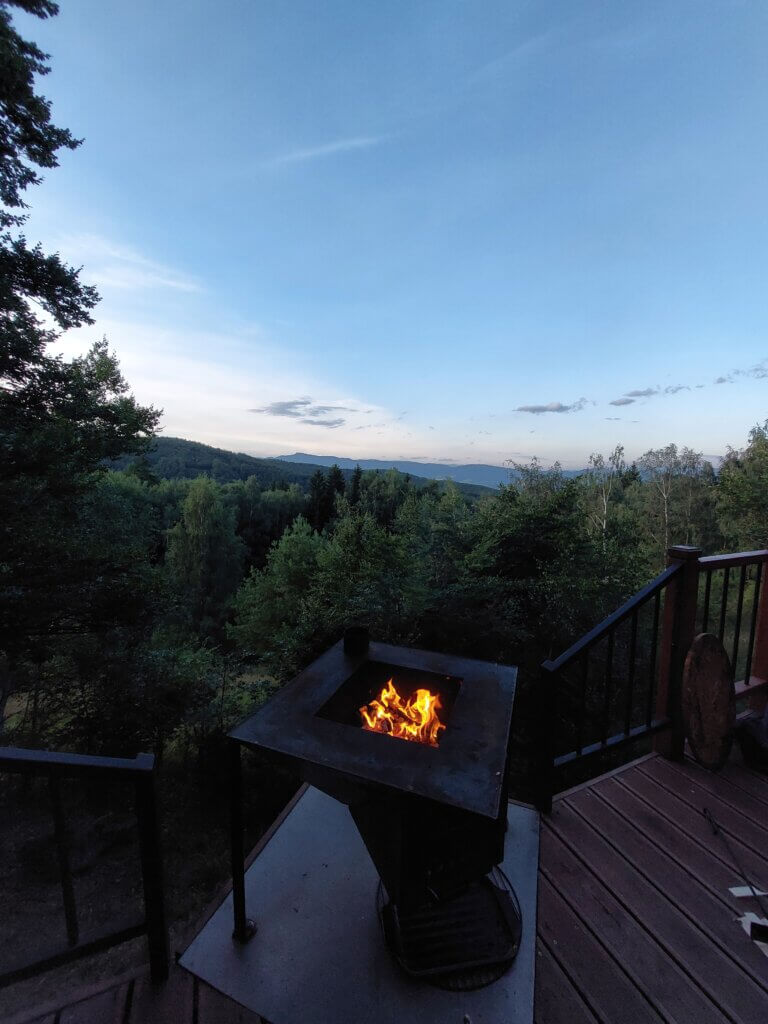 Fire pit on the edge of a wooden terrace overlooking trees and mountains