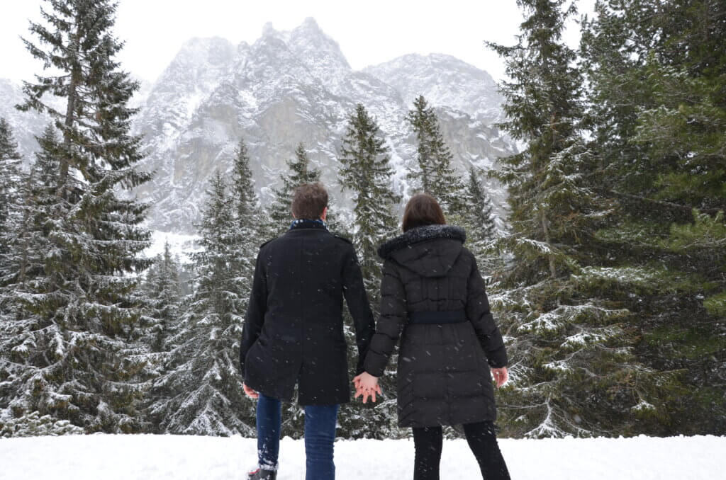 Mirka and Daniel facing away from the camera towards a big snowy mountain with a forest below