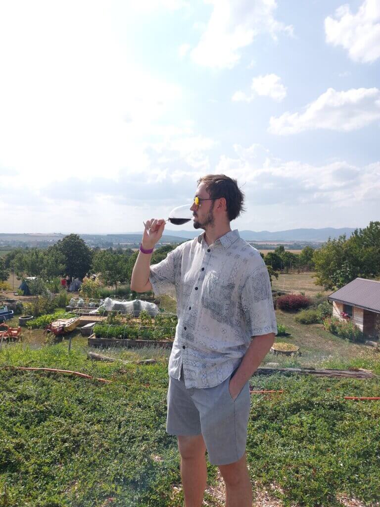 Daniel drinking from a glass of red wine with the Slovak countryside behind him