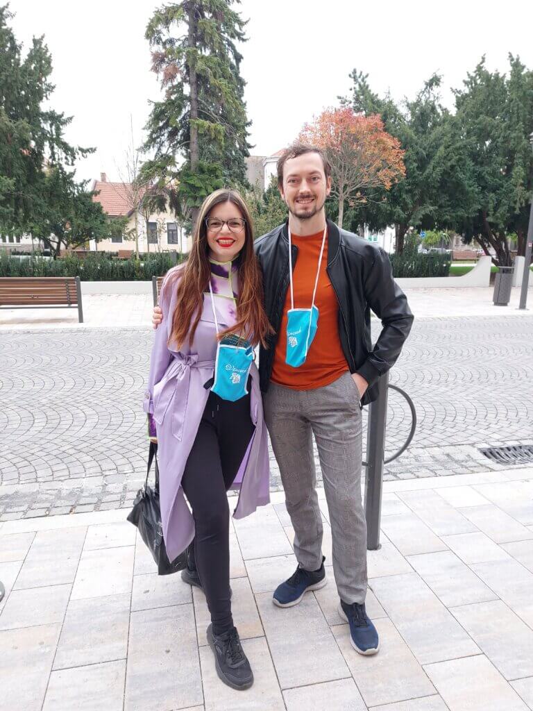 Mirka and Daniel at the start of the unlimited wine drinking event, wearing little bags around their necks with a wine glass and a map