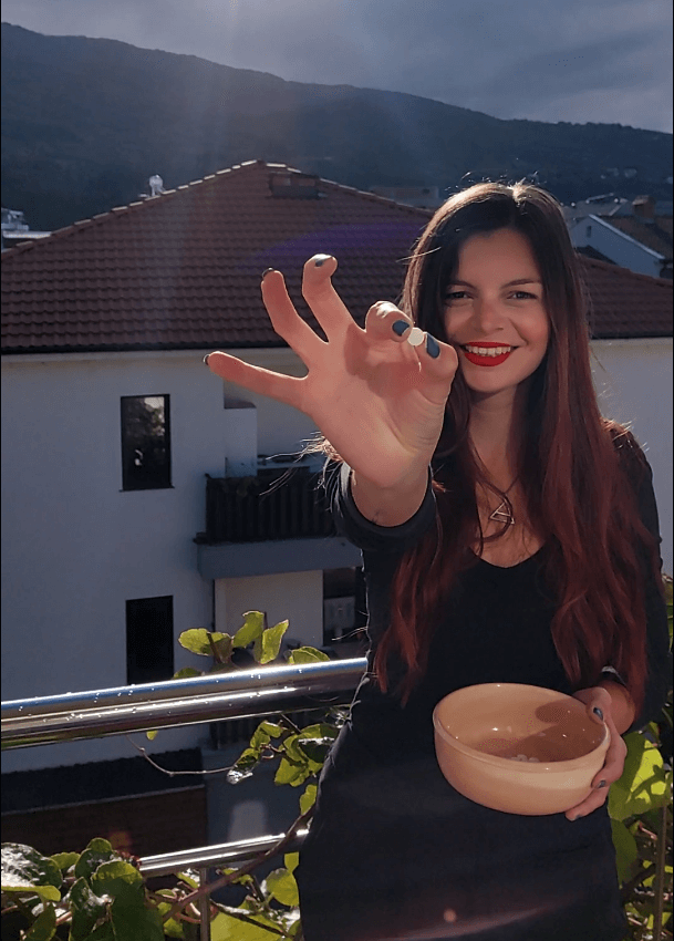 Mirka holding up a little white round tablet to a camera with a view of mountains behind her