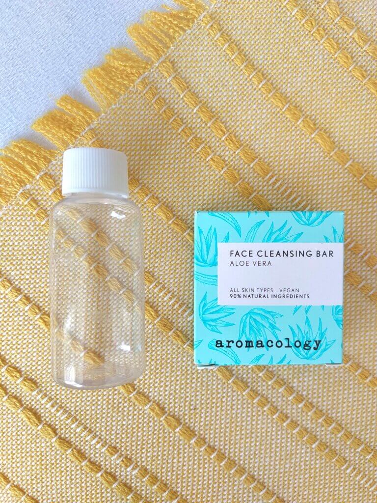 A small travel bottle for liquids next to a solid facial cleasing bar
