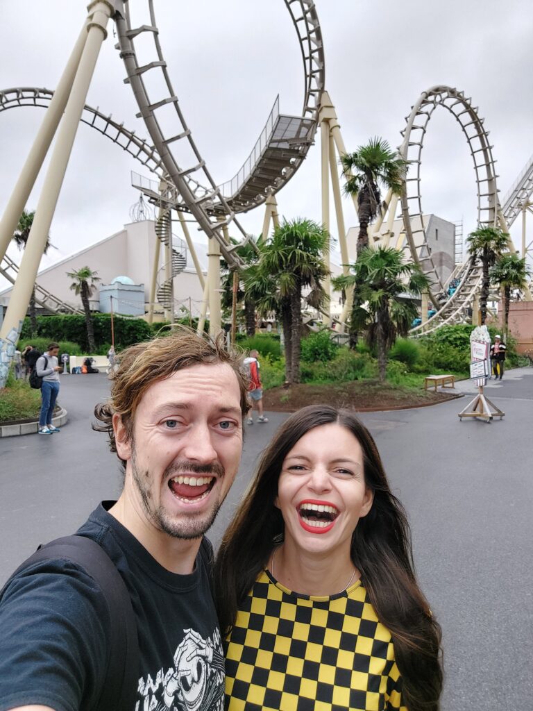 Mirka and Daniel taking a selfie in front of a rollercoaster in a theme park