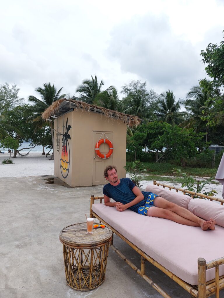Daniel lounging on a wicker sofa near a beach