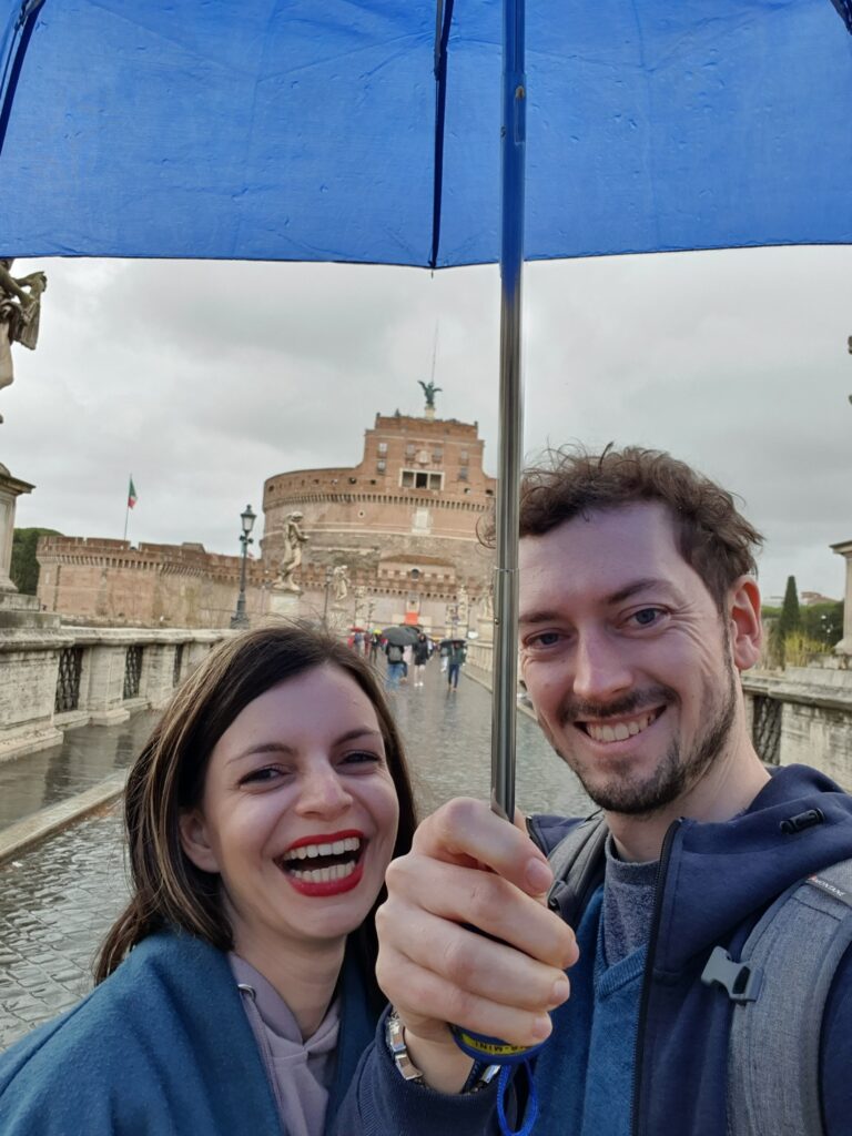 Mirka and Daniel taking a selfie under an umbrella in front of Castel Sant'Angelo