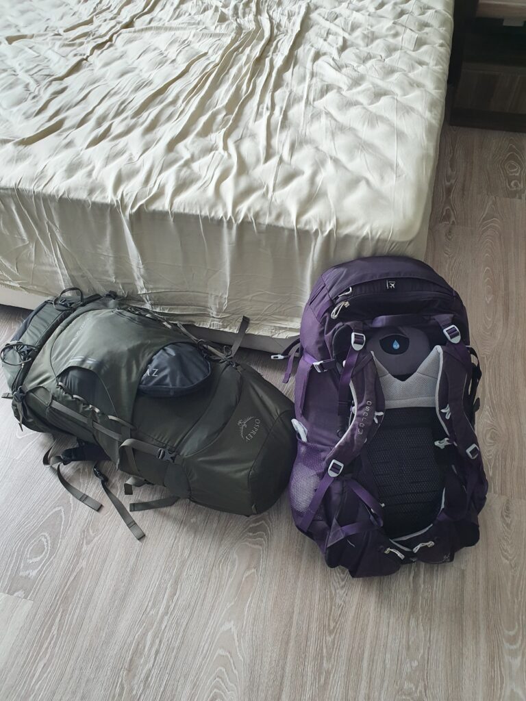 Two big Osprey backpacks lying on the floor next to a bed