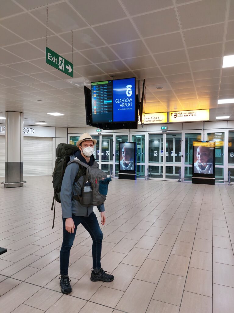 Daniel at an airport wearing two backpacks and a summer hat