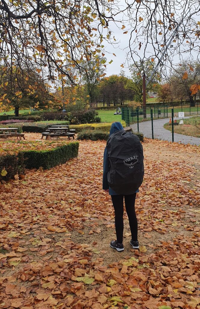 Mirka standing in a park with a big Osprey backpack on with a waterproof cover