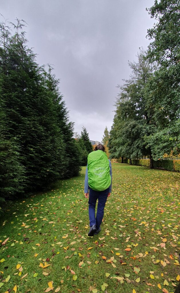 Daniel standing in a park with a big backpack in a bright green rain cover