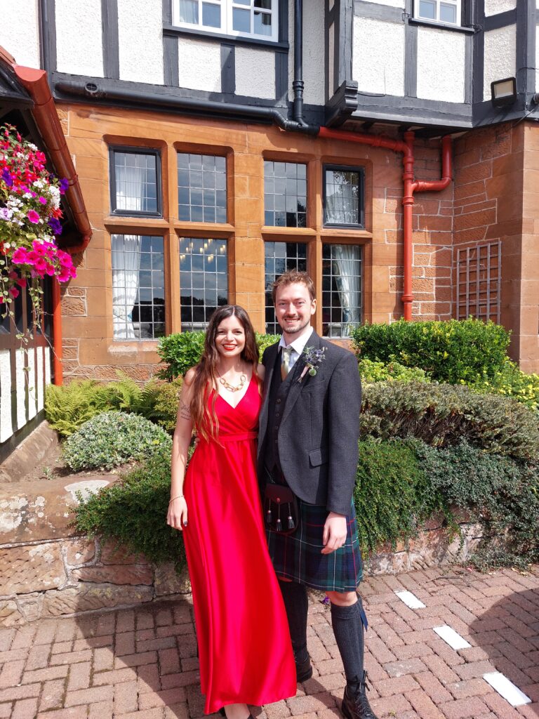 Mirka in a long red dress and Daniel in a kilt posing at a wedding