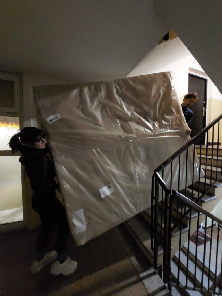 Two people carrying a massive mattress up the stairs