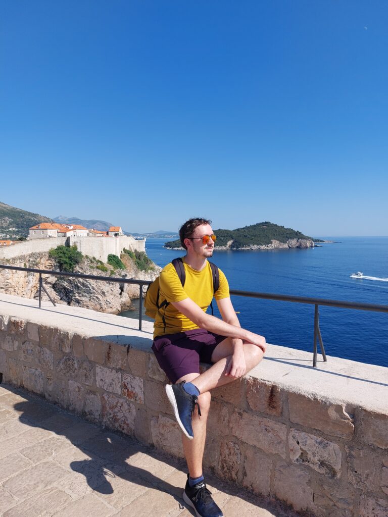 Daniel sitting on a wall with the sea behind him