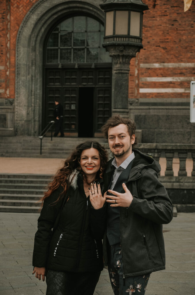 Mirka and Daniel holding up their hands with wedding rings outside of a town hall