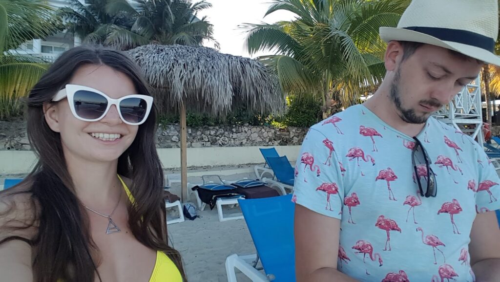 Mirka and Daniel taking a selfie at a beach with sun loungers