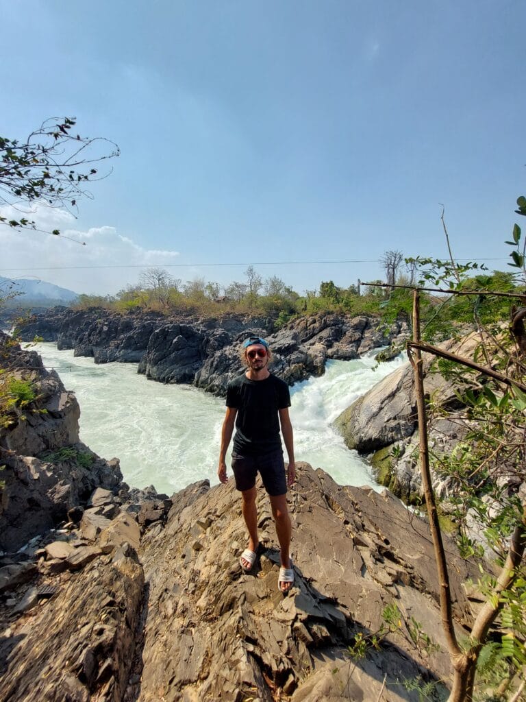 Daniel standing on a rock above a wild river wearing sliders