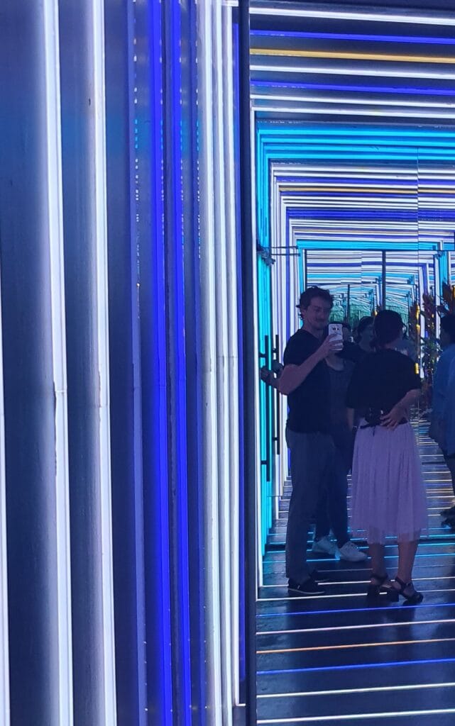 Mirka and Daniel standing in a blue-lit mirror corridor wearing TOMS and black heel sandals - not the best shoes for long-term travel