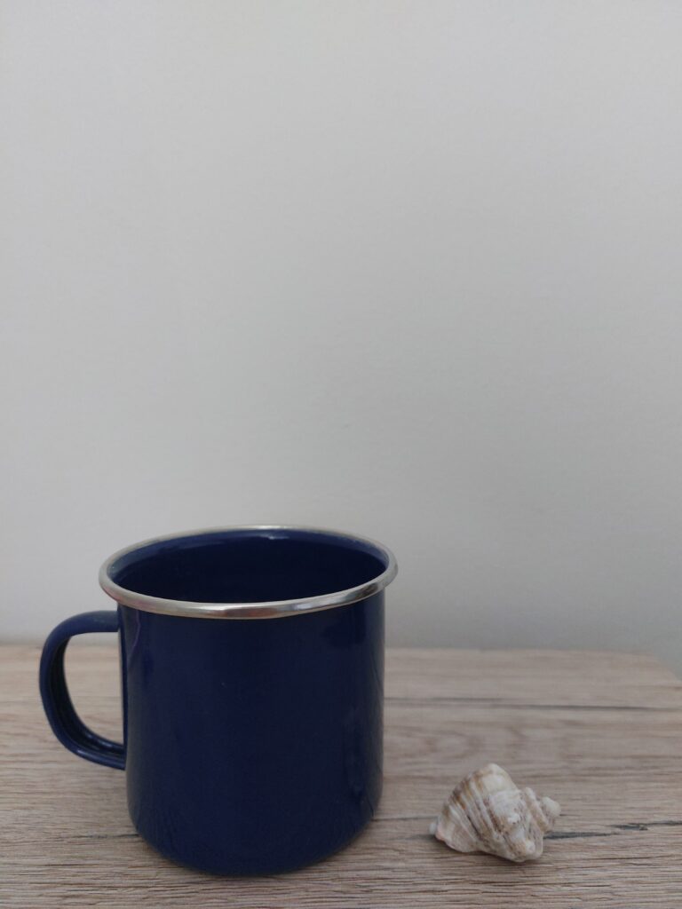 Small blue camping mug next to a small shell