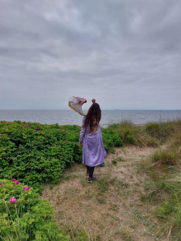 Mirka standing on a hill facing the sea with dark clouds above her