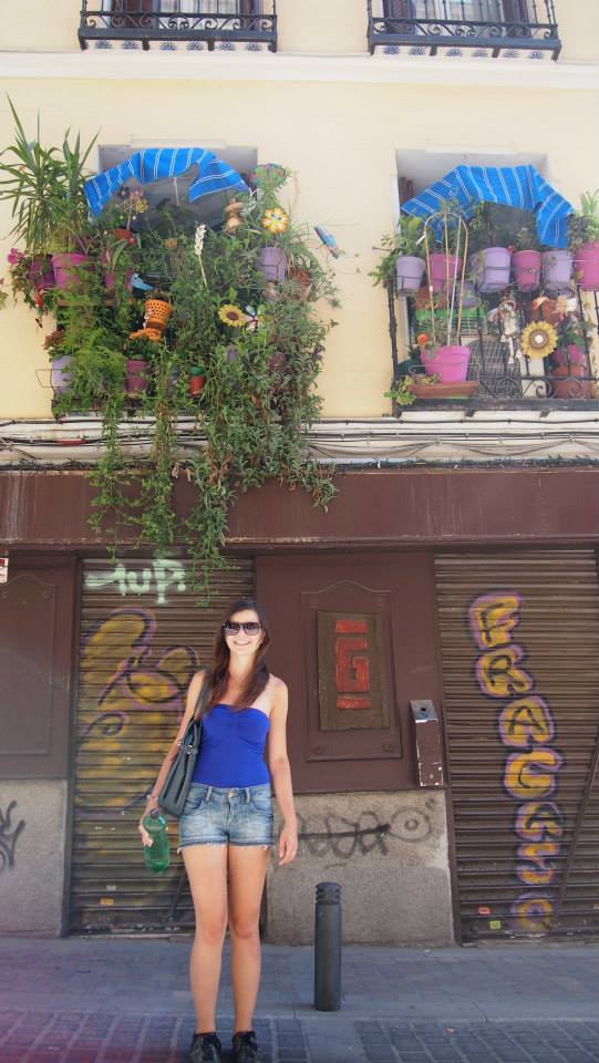 Mirka wearing summer clothes standing underneath balconies stuffed with plant pots