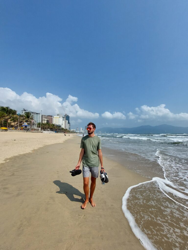 Daniel walking along the beach carrying two sets of sliders and a water bottle
